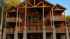 A large, multi-story lodge with a wooden exterior, multiple balconies, and a stone foundation. - Luxury Stowe Home w/ Sauna & Hot Tub (Stowe)
