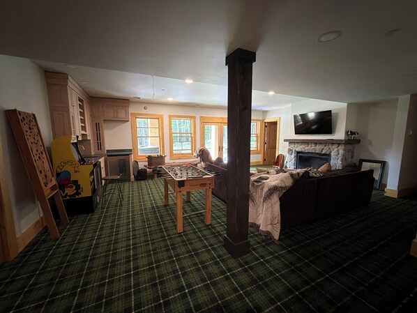 A spacious living area with a foosball table, a fireplace, and a television mounted on the wall.
