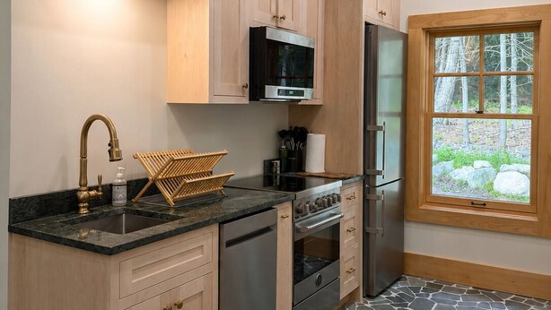 A kitchen with wooden cabinets, a stainless steel refrigerator, a microwave, and a stone-patterned floor. - Luxury Stowe Home w/ Sauna & Hot Tub (Stowe)