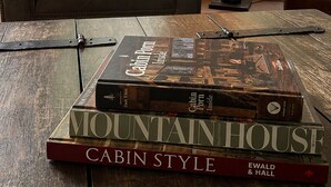 Un fauteuil en cuir, un coussin du Vermont, une lampe et une pile de livres sur une table en bois.