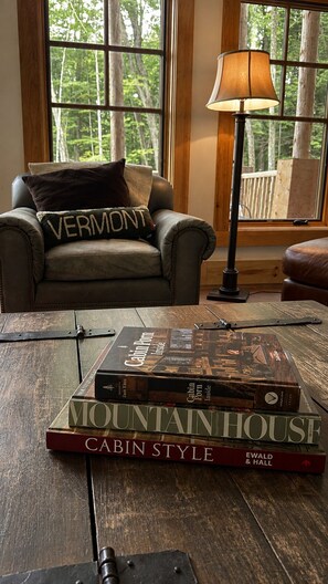 Un sillón de cuero con un cojín de Vermont, una lámpara y una pila de libros sobre una mesa de madera.