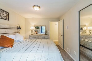 Ein Schlafzimmer mit einem Bett, Nachttischlampen, einem Nachttisch, einem Spiegel und einer Tür.