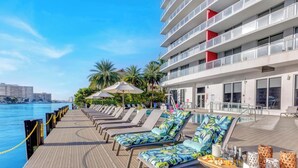 A poolside area with lounge chairs and umbrellas, a pool, and a building with balconies. - High-Floor Studio with Intracoastal Views (Hallandale Beach)