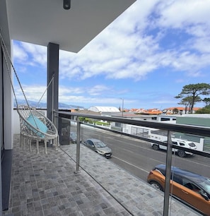 Un balcon donnant sur une rue, un fauteuil suspendu et un bâtiment avec un toit blanc.