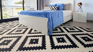 Een moderne slaapkamer met een groot bed, nachtkastje, lamp en uitzicht op de omgeving.