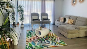Een woonkamer met een bank, twee fauteuils, een bijzettafeltje en een kleurrijk vloerkleed.