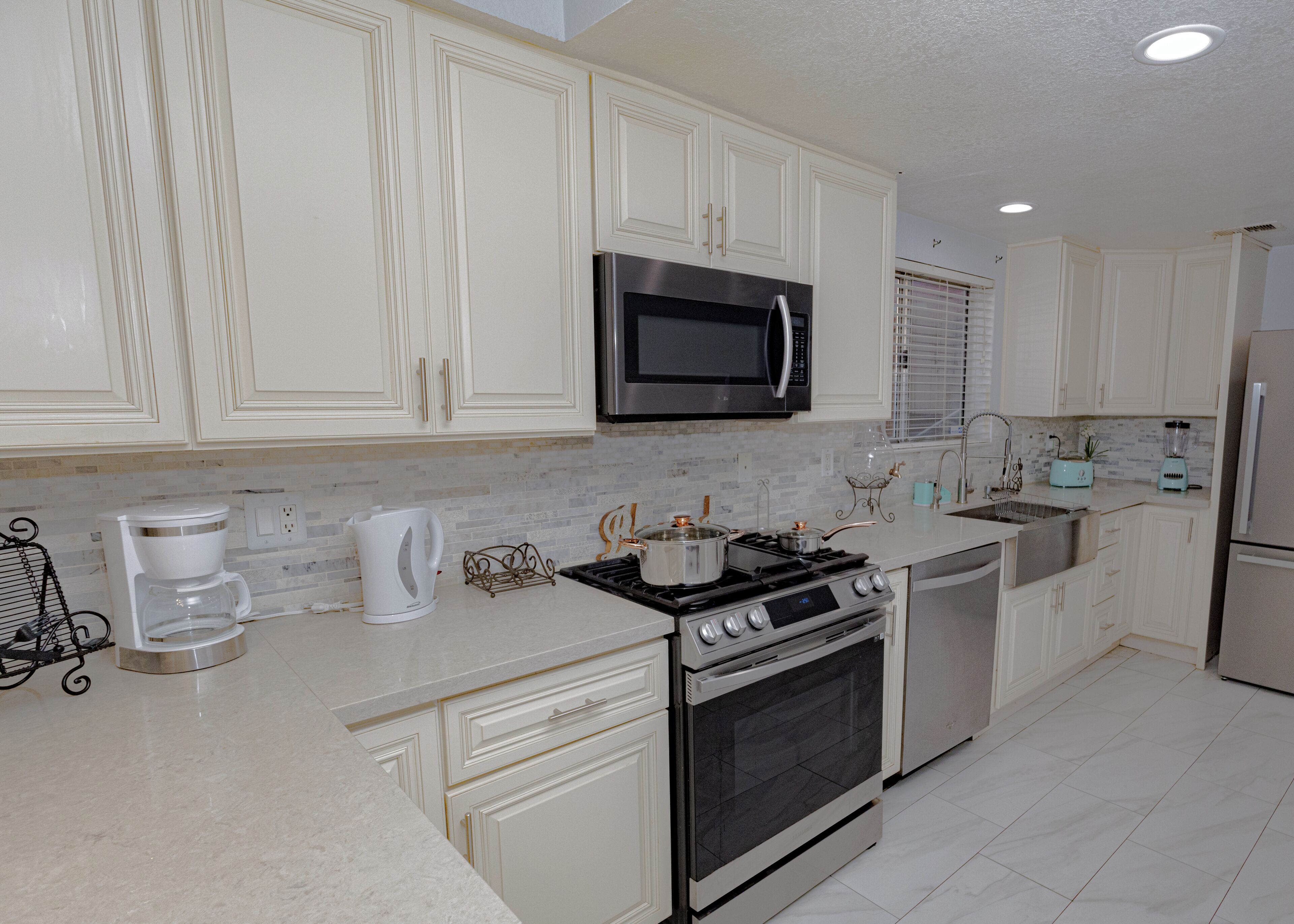 A modern kitchen with white cabinetry, a stainless steel stove, a microwave, and a refrigerator.