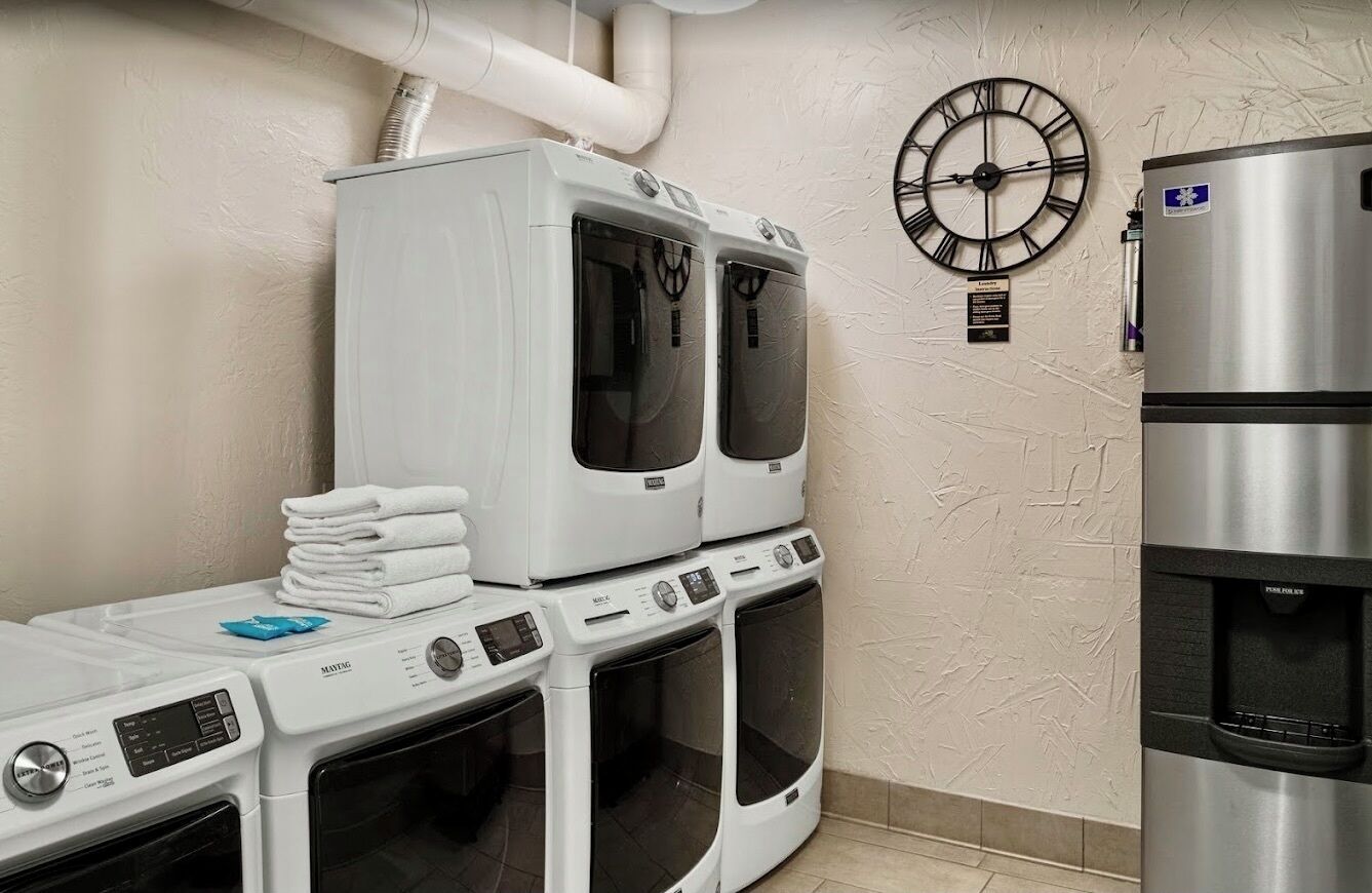A laundry area with stacked dryers, a water dispenser, and a clock on the wall.