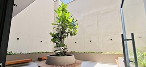 Un jardín interior moderno con un macetero central, bancos y una vista despejada del cielo.