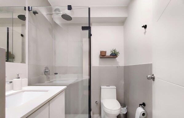 A modern bathroom with a glass shower enclosure, a toilet, and a sink with a mirror. - Luxe 1BR apartment in vibrant Miraflores! (Miraflores)
