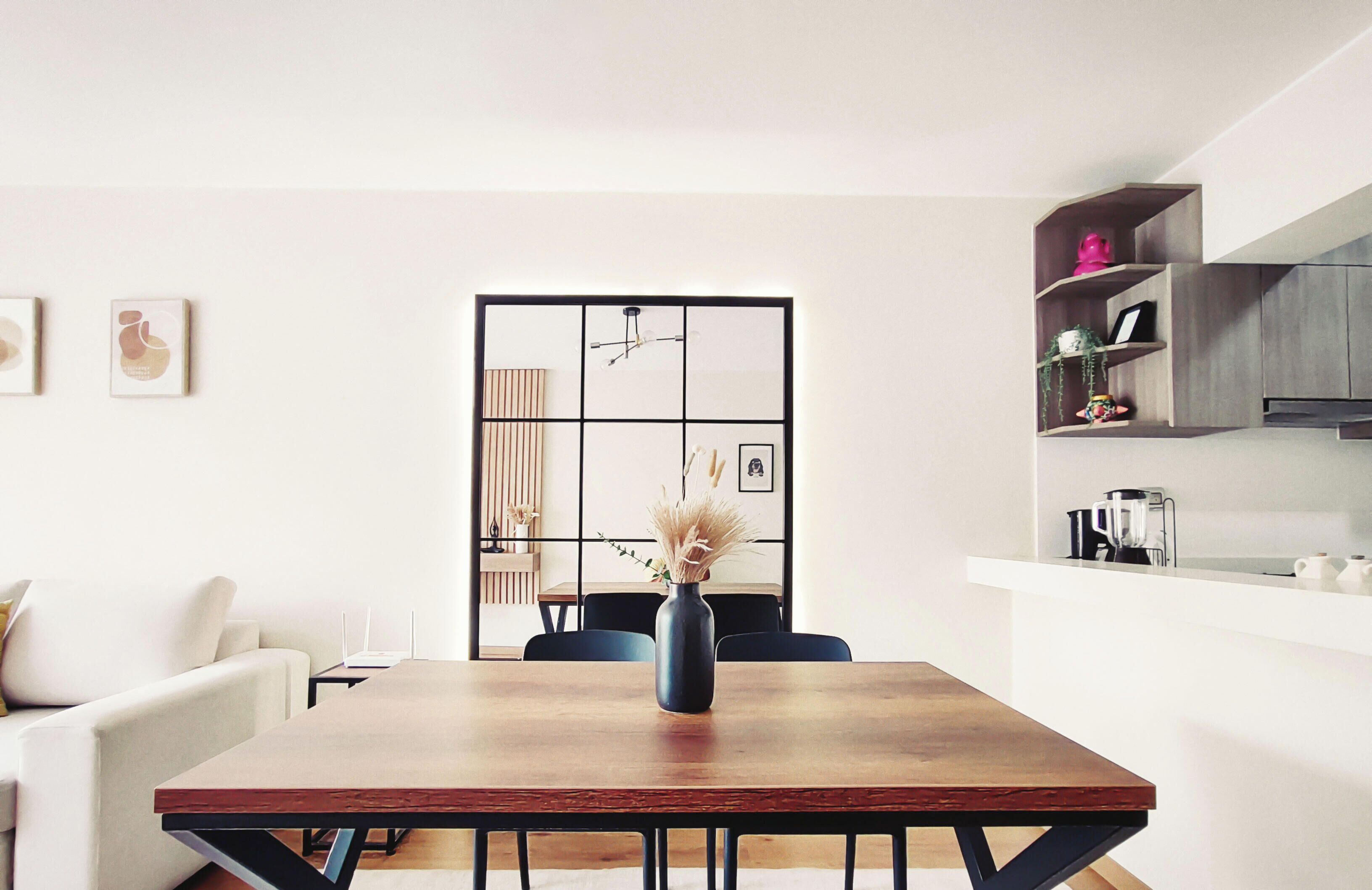 Un espacio habitable moderno con una mesa de comedor, sillas, un sofá, una zona de cocina y un jarrón decorativo.