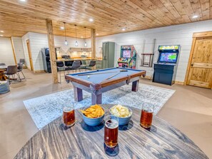 Ein Billardtisch mit Snacks und Getränken, eine Küchenzeile und Spielautomaten.