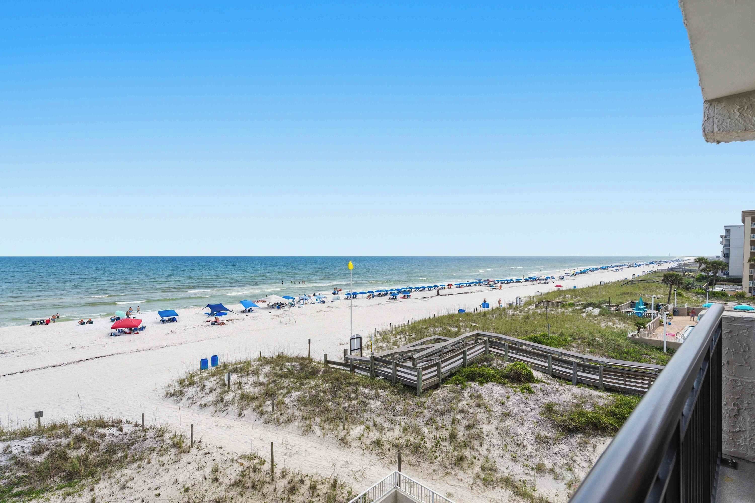 A beach view with a wooden boardwalk, beach umbrellas, and a flag.