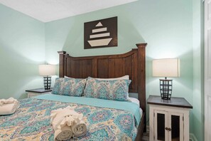 A bedroom with a bed, two bedside tables with lamps, a wall-mounted artwork, and a rolled towel on the bed. - Beachfront Paradise with Stunning Gulf Views, Island Echo Condo (Fort Walton Beach)