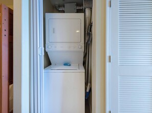 A compact laundry room with a washing machine and dryer, a wooden door, and a white wall. - Disney Dreams Apartment Amazing Lake Views! (Orlando)