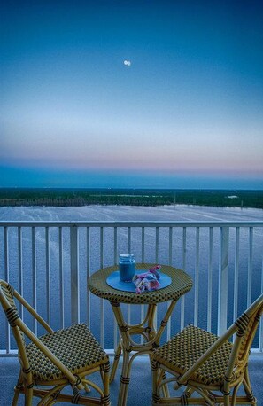 A balcony with two wicker chairs and a small round table, overlooking a beach and ocean. - Disney Dreams Apartment Amazing Lake Views! (Orlando)