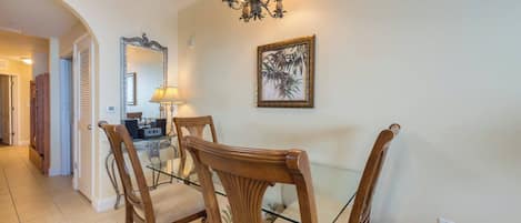 A dining area with a glass table, wooden chairs, a chandelier, a framed picture, and a door leading to another room.