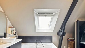 Un baño moderno con tragaluz, bañera y tocador con lavamanos.