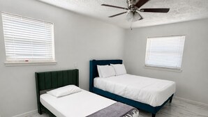 Un dormitorio con dos camas, ventilador de techo y suelo de mármol blanco.