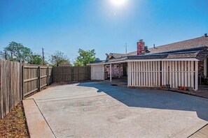 A backyard with a concrete patio, a wooden fence, and a covered area with a roof. - Villa Montalvo | Luxury retreat + pool table | Piano (Odessa)