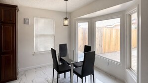 Un comedor con mesa y sillas de vidrio, una lámpara de techo y ventanas con vista a una cerca de madera.