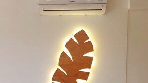 A bed with patterned bedding, a wall-mounted illuminated leaf design, and a ceiling air conditioner. - Bamboo Suite for 2 people, FREE parking (Rapallo)