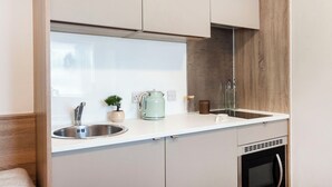 A modern kitchen with a stainless steel sink, a kettle, a small potted plant, and a built-in oven. - Student Only Berkshire House (Reading)