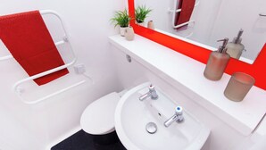 A bathroom with a white sink, two faucets, a red towel, a small plant, and a mirror with a red frame. - Student Only Berkshire House (Reading)