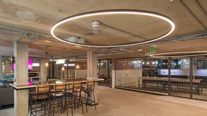 A modern bar area with a circular light fixture, bar stools, and a seating area with a sofa. - Student Only Berkshire House (Reading)