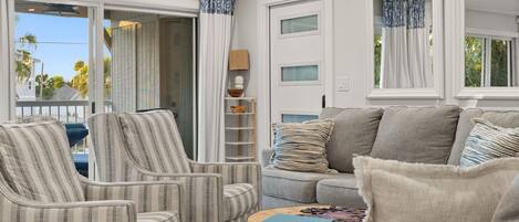 A living room with striped armchairs, a grey sofa, a small table with a book, and a door with a window.
