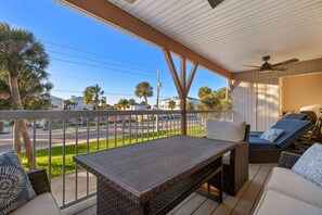 A covered outdoor seating area with a table and chairs, overlooking a street with palm trees and buildings. - Interlaken on the Coast - Beach Escape Awaits - Modern 2 Bedroom/2 Bathroom (Indian Rocks Beach)