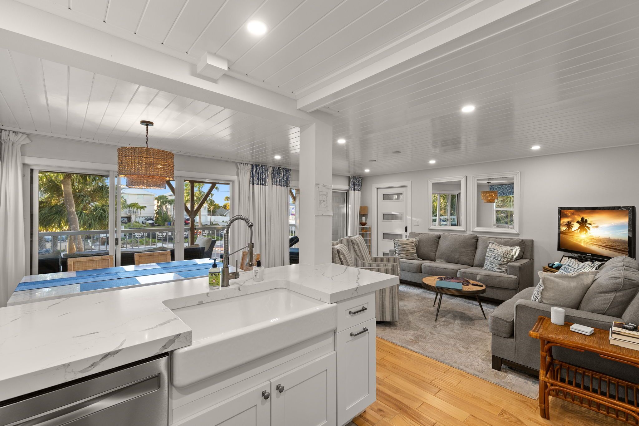 A modern kitchen with a white countertop and a dining area with a grey sofa and a coffee table.
