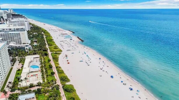 Ein Strand mit einem Hotel links, klarem blauen Wasser und einem wolkenlosen Himmel.