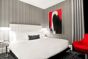 Ein modernes Hotelzimmer mit einem großen Bett, einem roten Sessel und einem an der Wand hängenden Kunstwerk.