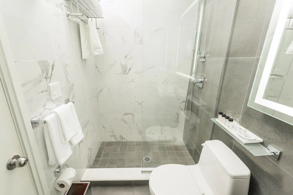 Un baño moderno con cabina de ducha de vidrio, inodoro y zona de lavamanos con artículos de aseo.