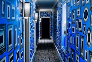 A hallway with patterned walls and a patterned carpet, leading to a dark doorway. - Deluxe King | Moderne | Steps to Times Square | Near Central Park (New York)