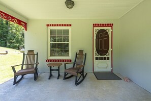 Eine Veranda mit drei Schaukelstühlen, einem kleinen Tisch und einer Tür mit dekorativer Verzierung.