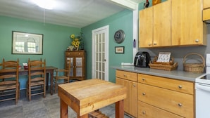 Een keuken met houten kastjes, een eettafel, stoelen, een klok en een vaas met zonnebloemen.