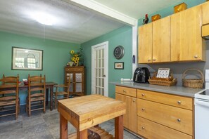 A kitchen with wooden cabinets, a dining table, chairs, a clock, and a vase with sunflowers. - Little Rock Creek Cottage on Trout Stream (Bakersville)