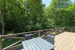 A wooden deck with a table and chairs, surrounded by a forested area. - Little Rock Creek Cottage on Trout Stream (Bakersville)