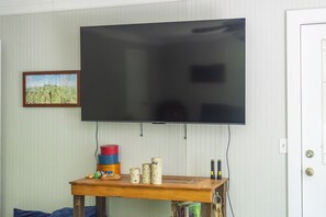 A room with a mounted flat-screen TV, a wooden table with various items, and a framed picture on the wall. - Little Rock Creek Cottage on Trout Stream (Bakersville)