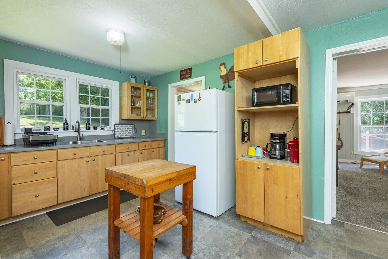 A kitchen with wooden cabinets, a white refrigerator, a wooden table, and a microwave on a shelf.