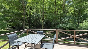 Een terras buiten, met een tafel en stoelen, omgeven door een houten balustrade, gelegen in een bebost gebied.