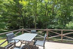 An outdoor deck with a table and chairs, surrounded by a wooden railing, set in a wooded area. - Little Rock Creek Cottage on Trout Stream (Bakersville)
