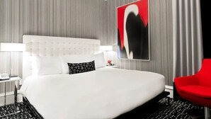 Ein modernes Hotelzimmer mit einem großen Bett, einem roten Sessel und einem an der Wand hängenden Kunstwerk.