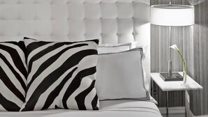 Ein Bett mit einer karopragigen Kopfteile, ein Zebra-Kissen, ein schlichtes Kissen, ein Nachttisch mit Lampe und eine Vase mit einer einzelnen Blume.