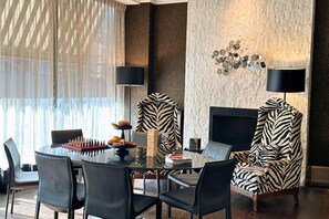 Ein moderner Essbereich mit einem Glastisch, schwarzen Stühlen und einem Ohrensessel mit Zebra-Muster.