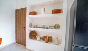 Ein Zimmer mit Holztür, weißen Wänden und einem Regal mit verschiedenen Gegenständen, darunter ein weißer Krug, eine Holtschüssel und eine Keramikkanne.