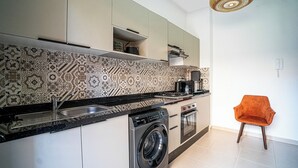 Una cocina moderna con un salpicadero estampado, lavadora integrada y un pequeño comedor con una sola silla naranja.