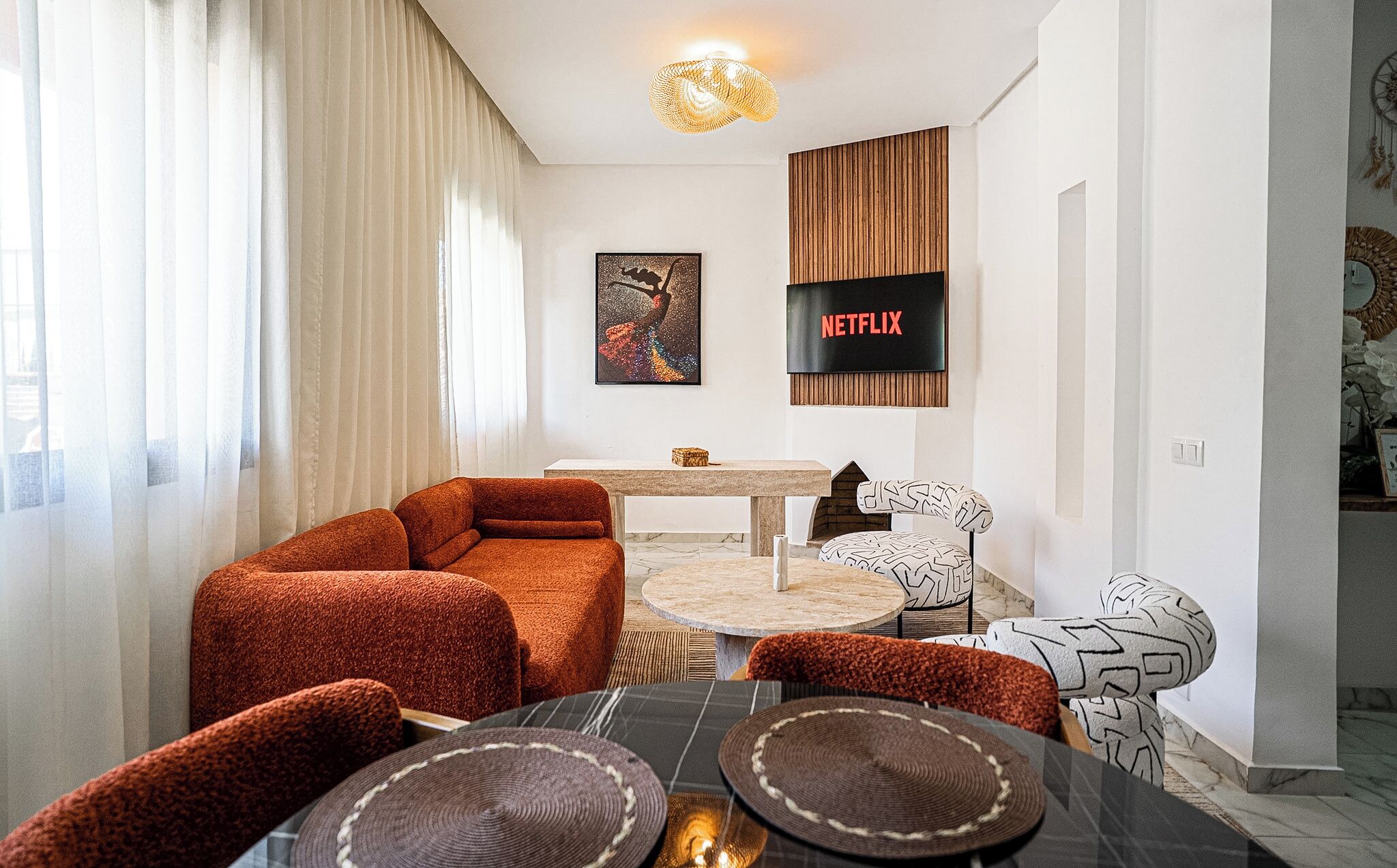 Una sala de estar moderna con un sofá, una mesa redonda y un sillón estampado. Un televisor de pantalla plana está montado en la pared.
